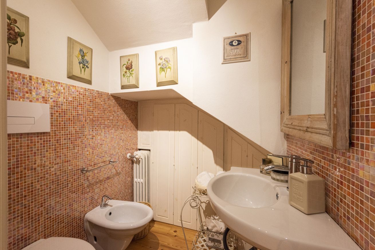 A bathroom with a white sink, a bidet, a towel rack, and a tiled wall with floral artwork.