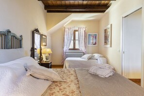 Une chambre avec deux lits, une tête de lit en bois, une table de chevet avec une lampe, un radiateur et une fenêtre avec des rideaux.