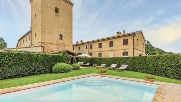 Un patio con piscina, una torre alta y un edificio con múltiples ventanas.