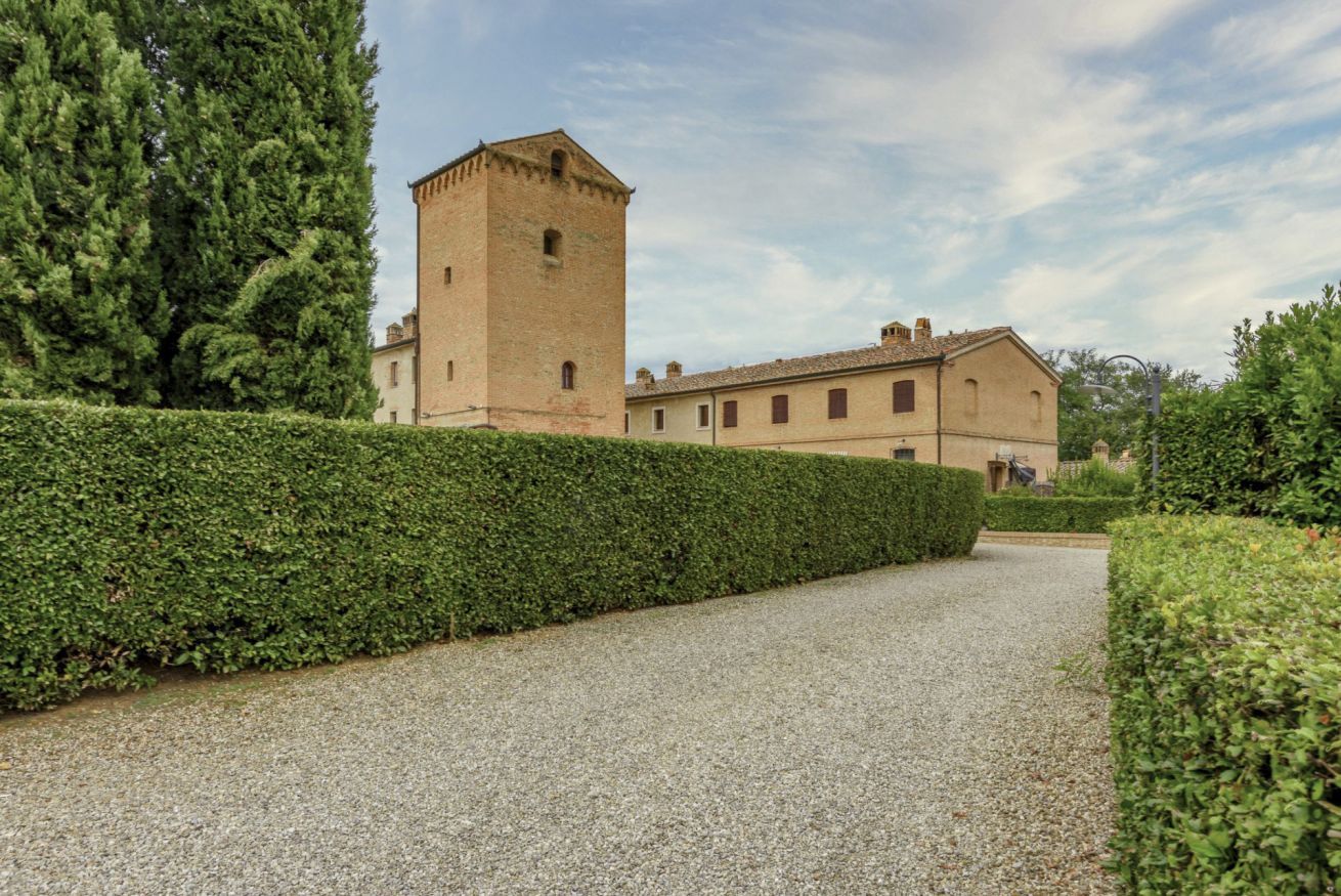 A building with a tower, a gravel path, and a hedge.