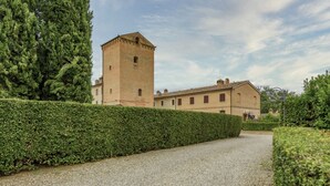 Un edificio con una torre, un sendero de grava y un seto.