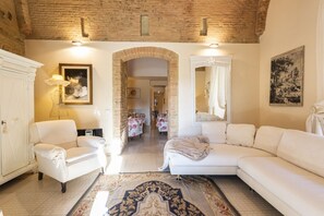 Una habitación con un sillón blanco, un sofá, un tapiz estampado, una chimenea y un espejo.