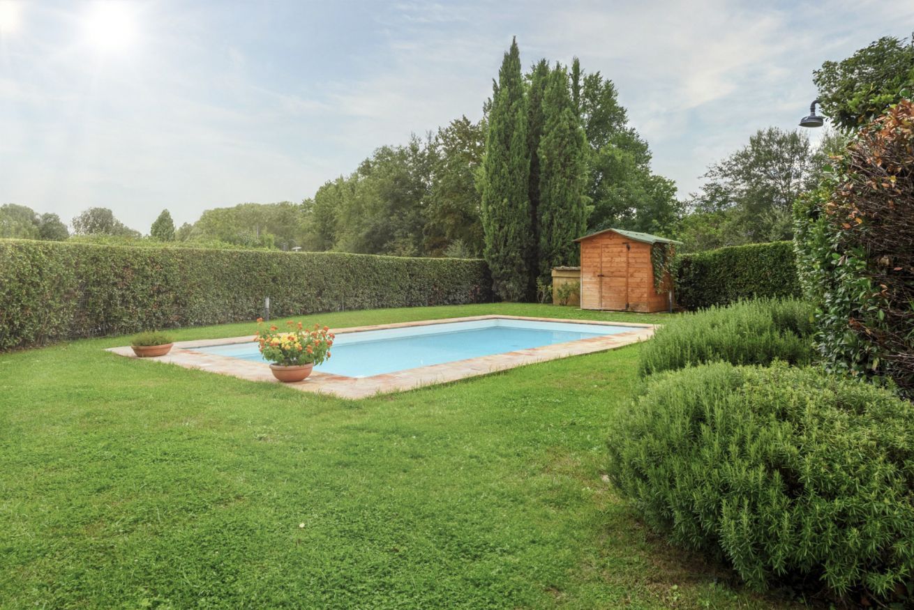 Una piscina rectangular con muelle de madera, rodeada de césped cuidado y setos.