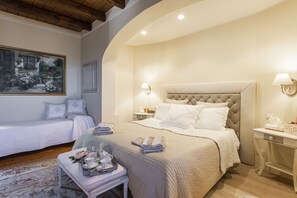 Un dormitorio con una cama grande, una cama más pequeña, una mesita de noche, una lámpara, un cuadro en la pared y una ventana.