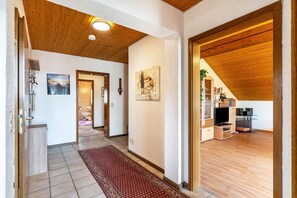 Ein Flur mit Holzboden, einem roten Teppich mit Muster, einer Holzzielung und einer TV-Konsole mit Fernseher und Regalen.