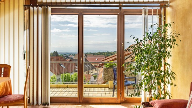 Ein Zimmer mit einer Schiebetür zum Balkon, einem Sessel, einer Couch und einem Blumentopf.