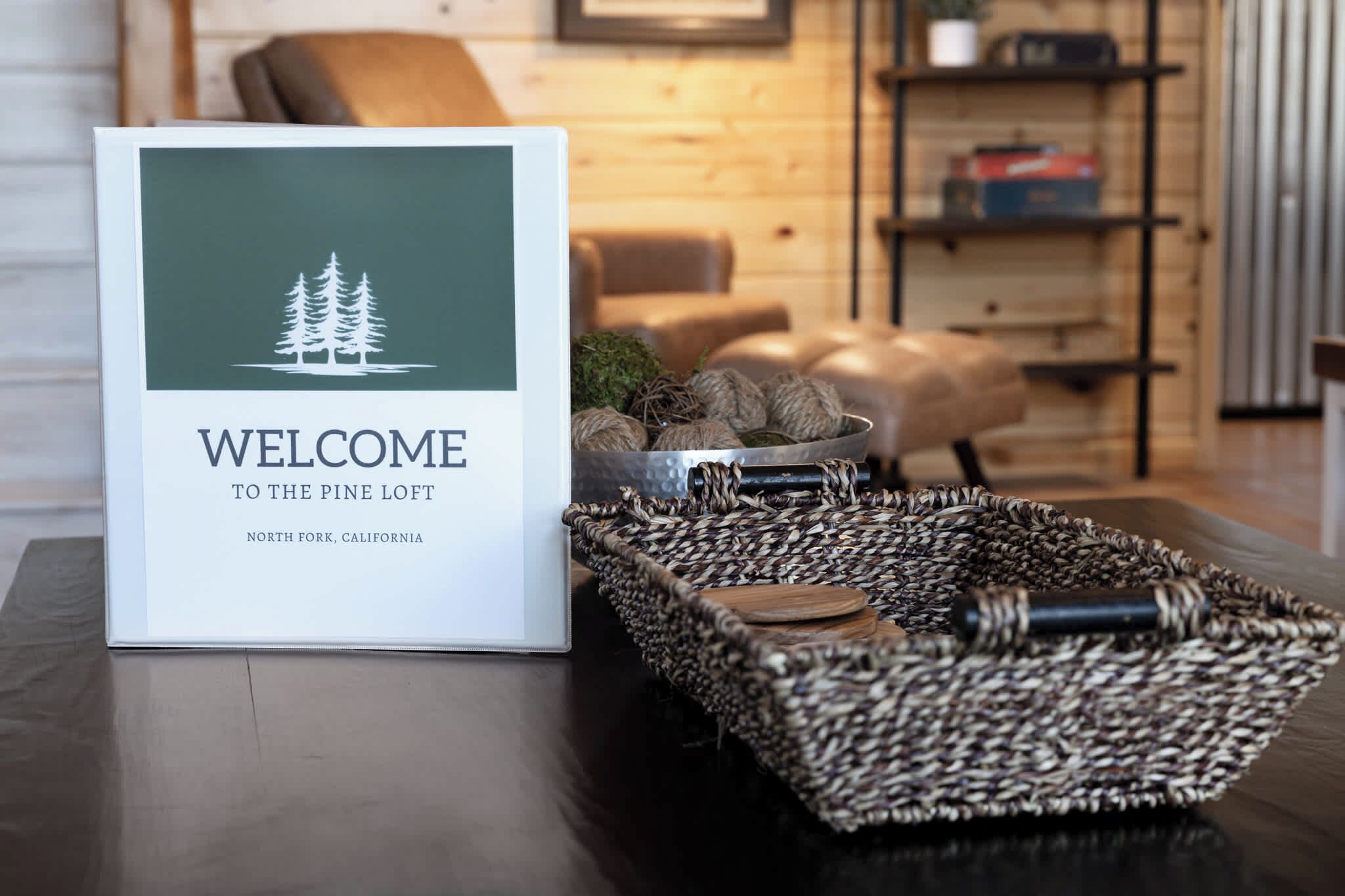 Placa de boas-vindas para o Pine Loft em North Fork, Califórnia, uma cesta de vime com itens decorativos e uma sala de estar aconchegante com sofá e mesa de centro de madeira.