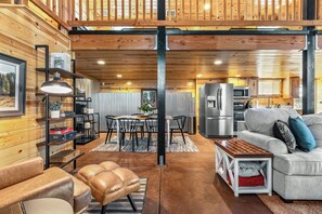 A spacious living area with a high ceiling, wooden walls, a dining table with chairs, a sofa, and a coffee table.