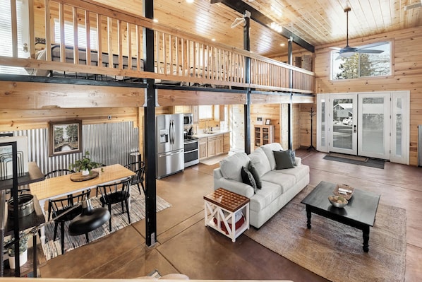 A spacious loft-style living area with a dining table, sofa, and a kitchen in the background.