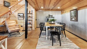 A wooden interior with a dining area featuring a table and chairs, a sofa, and a staircase. - The Pine Loft Family-Friendly Nature Retreat (North Fork)