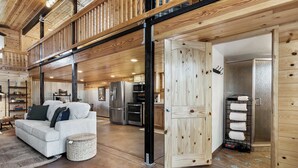 A spacious living area with a high ceiling, a white sofa, a woven ottoman, and a kitchen in the background. - The Pine Loft Family-Friendly Nature Retreat (North Fork)