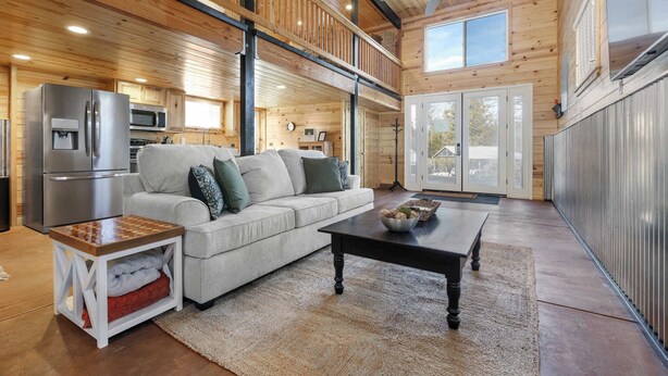 A spacious living area with a wooden ceiling, a sofa, a coffee table, and a refrigerator. - The Pine Loft Family-Friendly Nature Retreat (North Fork)