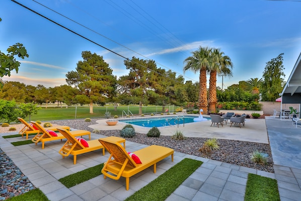 A backyard with a swimming pool, lounge chairs, and a patio area.