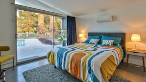 Une chambre moderne avec un grand lit, une porte-fenêtre coulissante donnant sur un espace extérieur et une petite table de chevet avec une lampe.