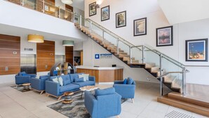 Un hall d’entrée moderne avec un comptoir d’accueil, des canapés bleus, un escalier et des tableaux encadrés accrochés aux murs.