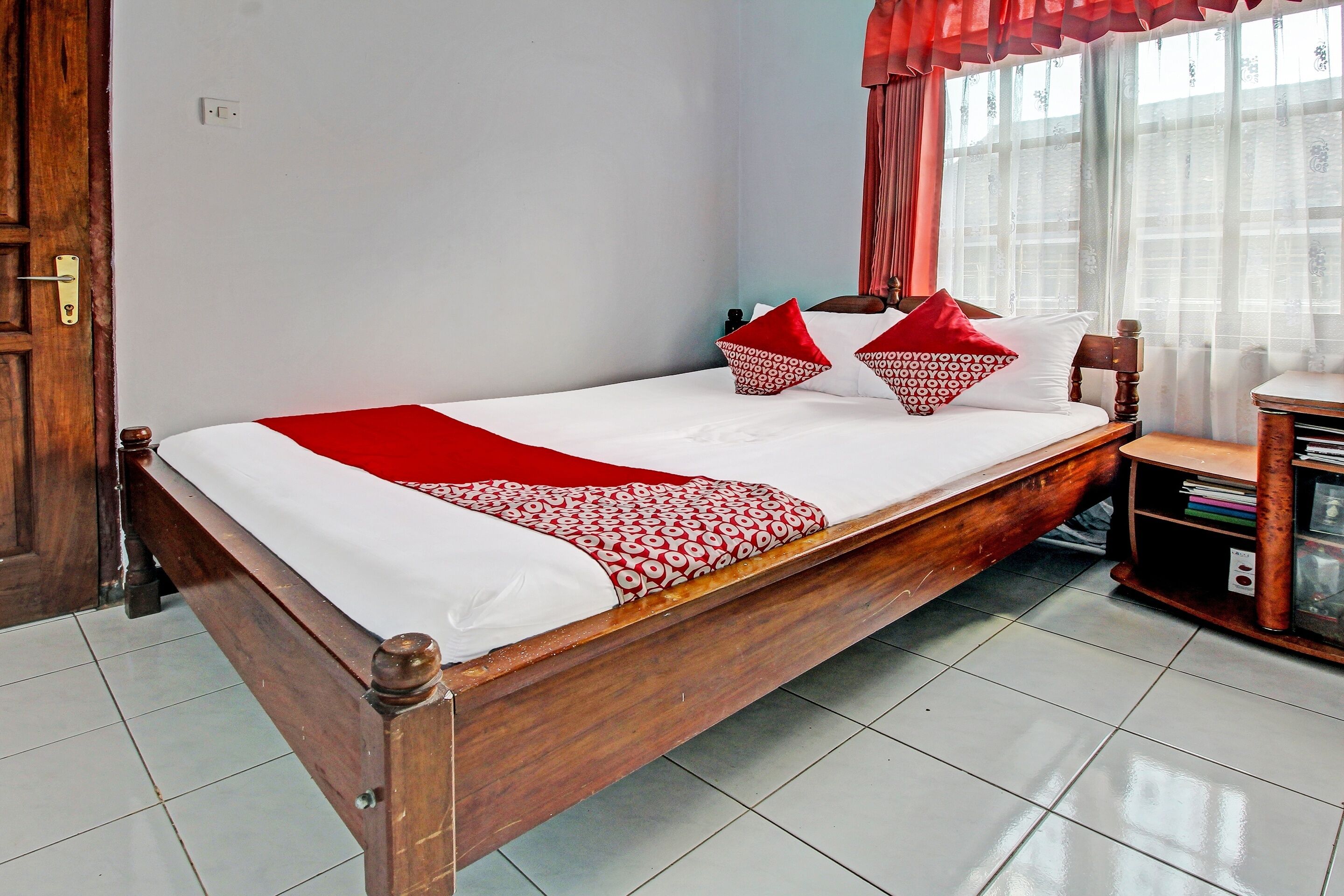 A single bed with a wooden frame, white bedding, and red and white patterned pillows.