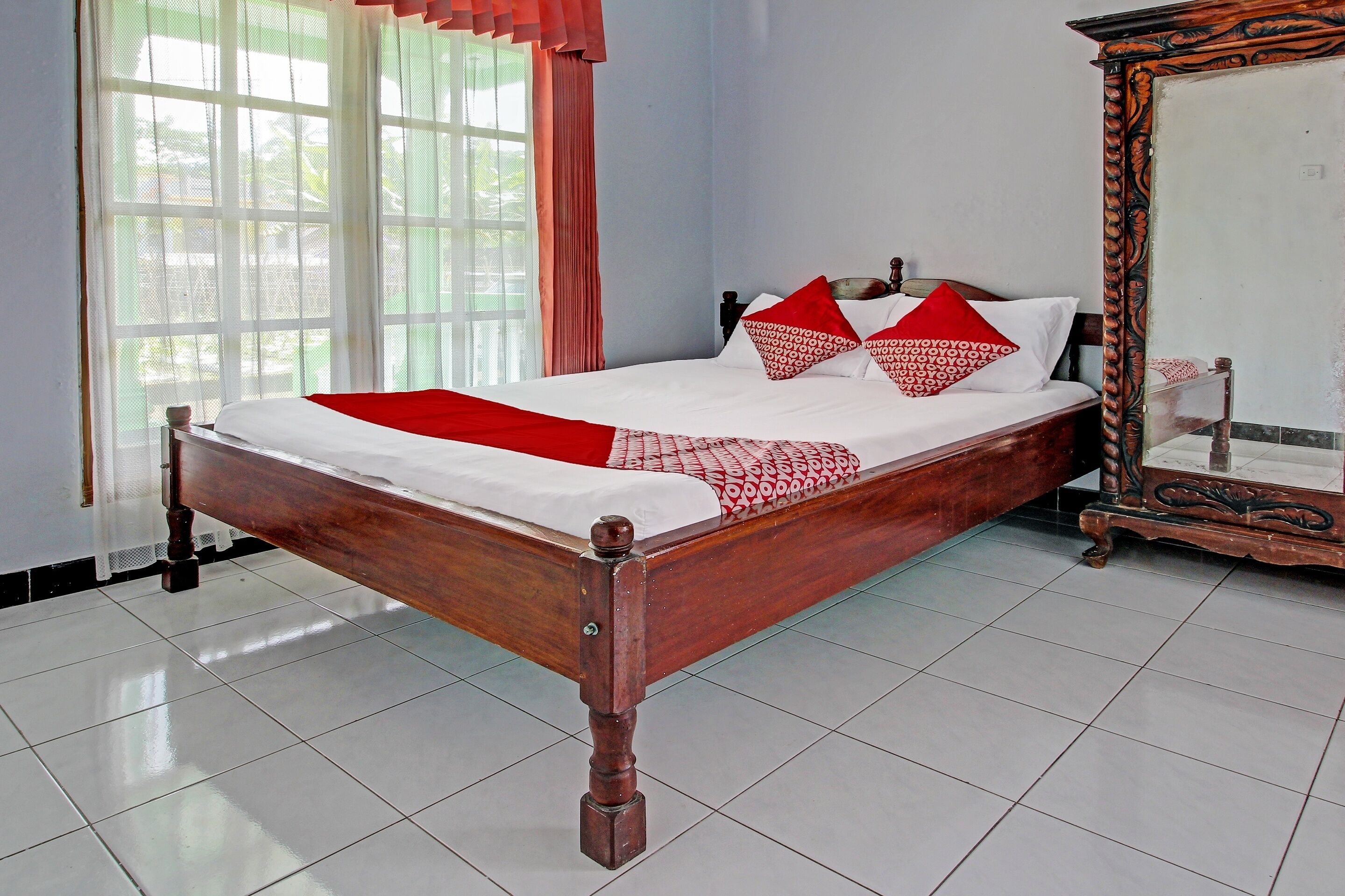 A neatly made bed with a wooden frame, white bedding, and red pillows.
