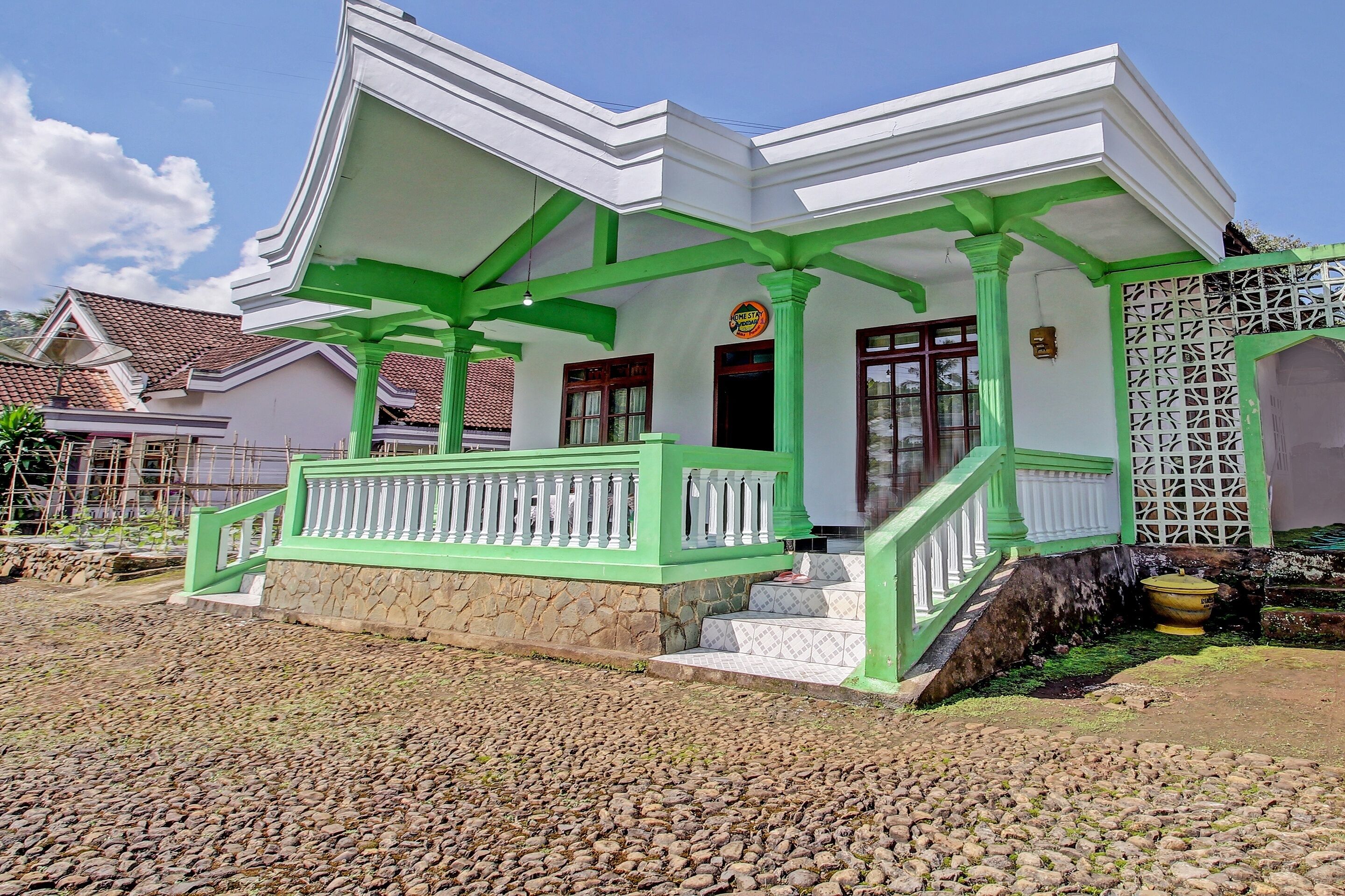 A white building with green accents, a stone foundation, and a staircase leading to the entrance.