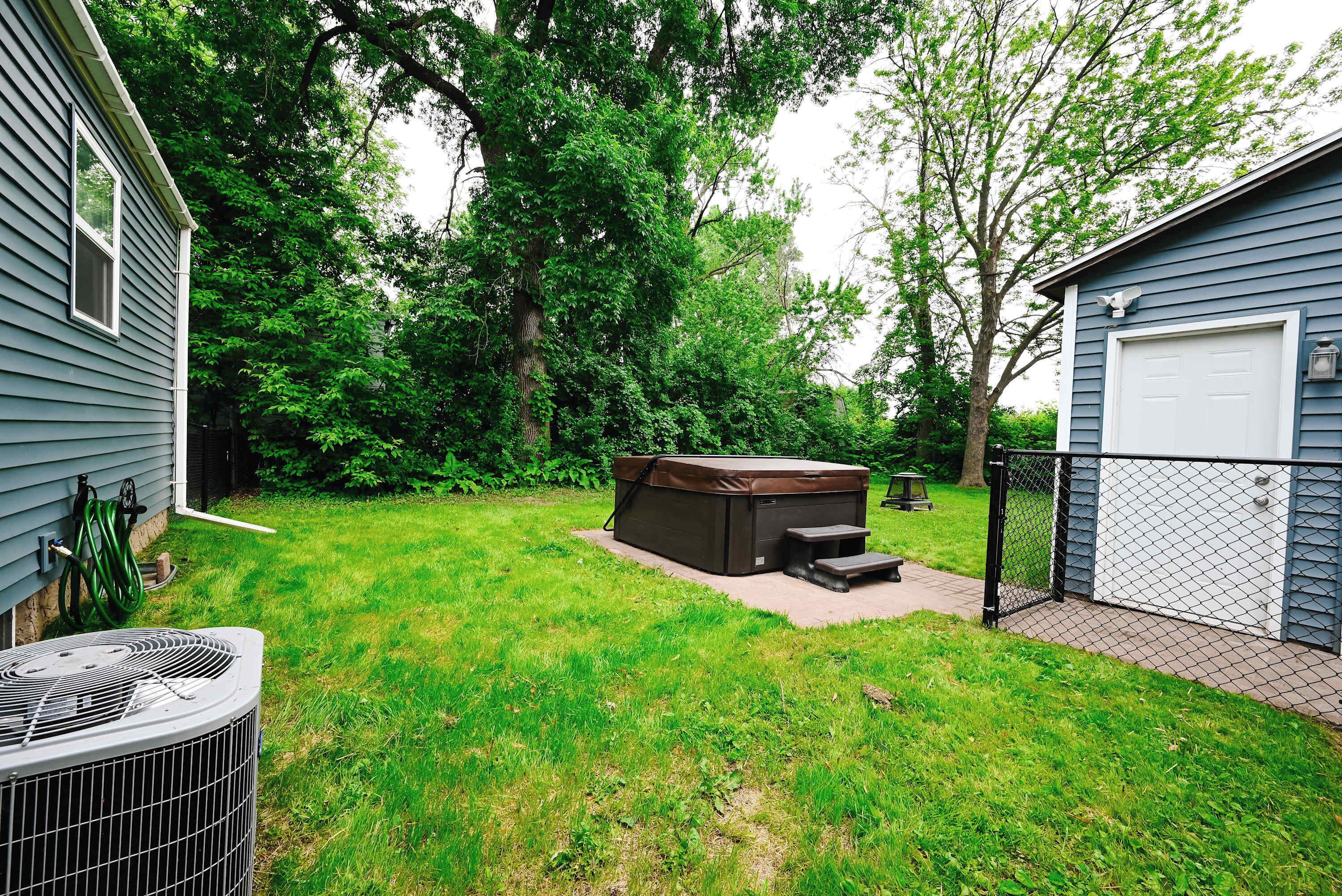 A backyard with a hot tub, a covered patio, and a fenced area.