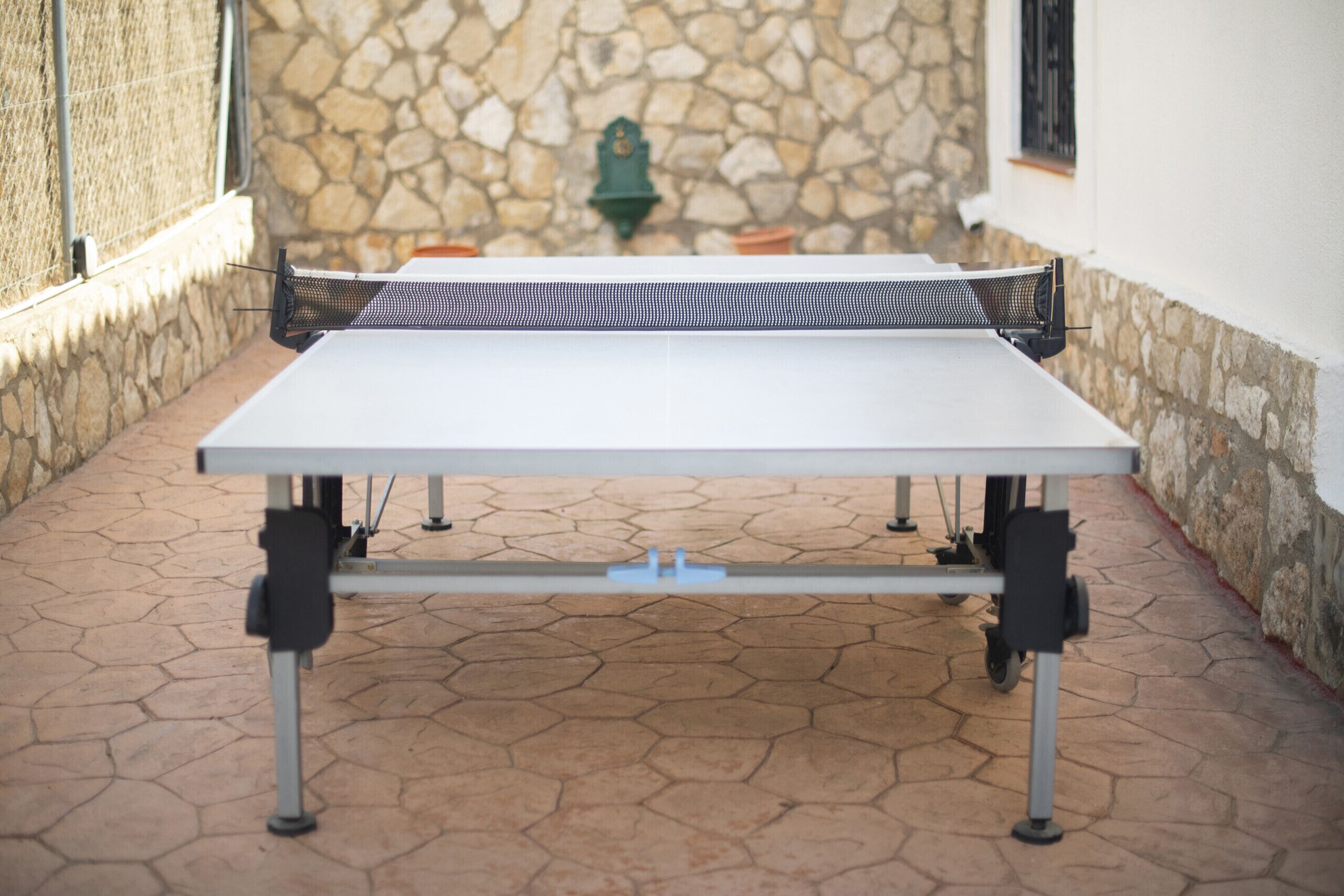 A ping pong table in an outdoor patio area with stone walls and a tiled floor.