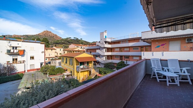 Un balcon avec des chaises blanches, une vue sur une colline et des bâtiments dotés de balcons.