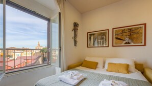 A hotel room with a large window, a bed with white bedding, two paintings on the wall, and a view of a cityscape. - Cozy Apartment in St. John - Yellow (Roma)