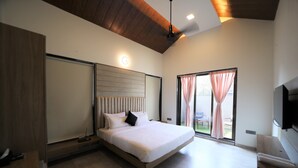 A modern bedroom with a large bed, a ceiling fan, a TV, and a sliding glass door to the outside. - Privystays Jks Private Villa (Alibag)