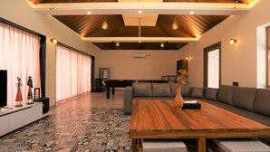A spacious living area with a wooden ceiling, a patterned floor, a large sofa, and a dining table. - Privystays Jks Private Villa (Alibag)
