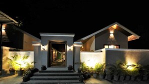 A modern house with a well-lit entrance, potted plants, and a visible pathway leading to the door. - Privystays Jks Private Villa (Alibag)