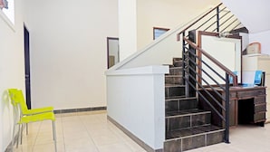 A staircase with a wooden handrail and black steps, leading to a landing with a desk and a chair. - OYO 91349  Karawaci Taman Permata 3 (Curug)