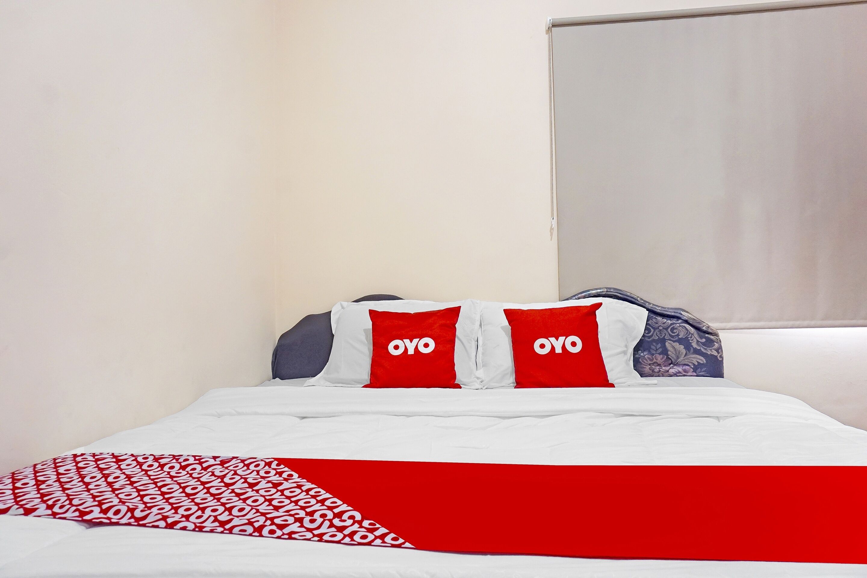 Habitación de hotel con cama, ropa de cama blanca y detalles rojos en almohadas y manta.