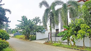A paved pathway flanked by lush greenery and a white building with a black fence. - OYO 91349  Karawaci Taman Permata 3 (Curug)