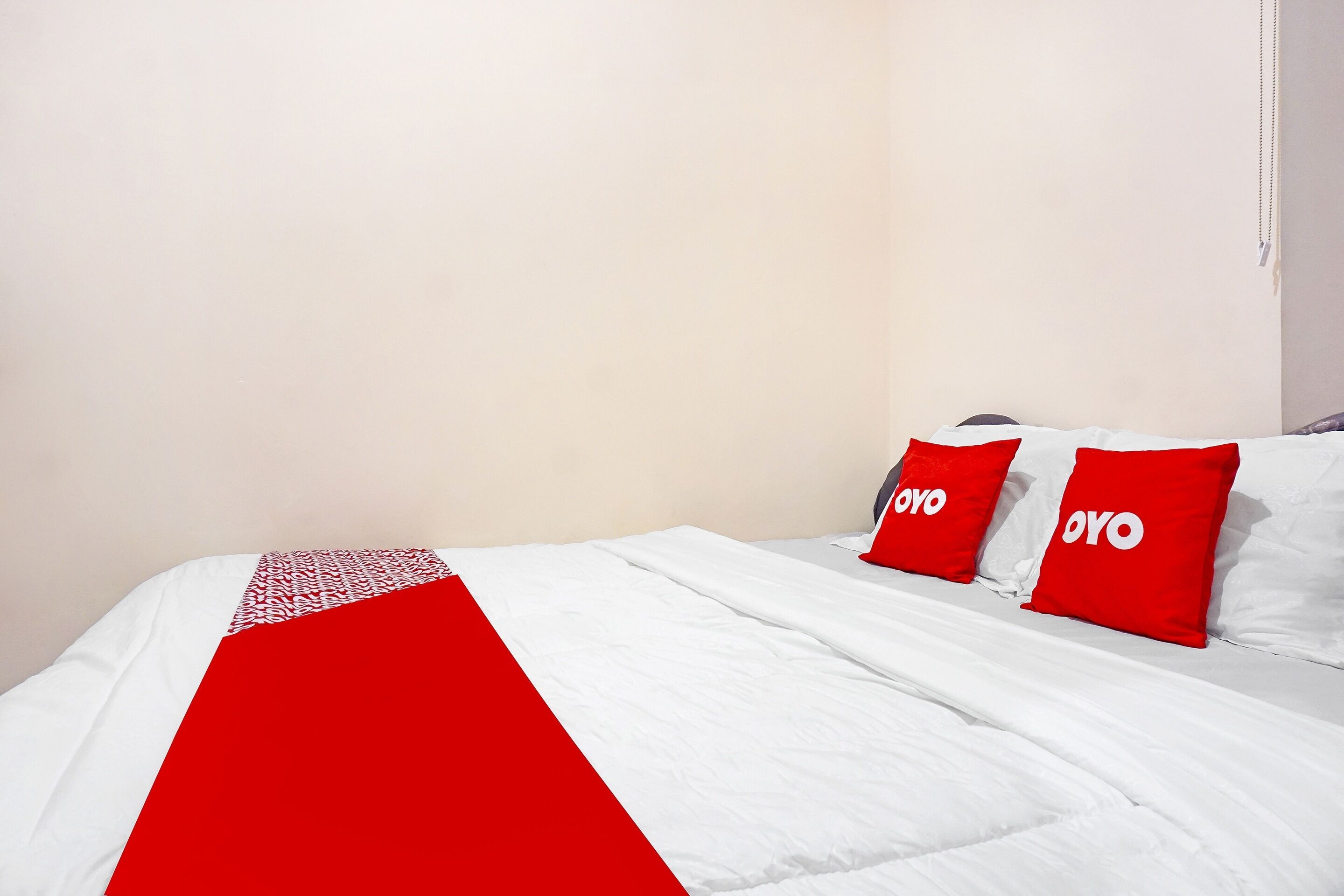 Een bed met witte beddengoed en twee rode kussens met de tekst 'OYO'.