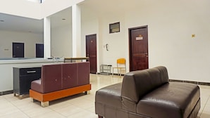 A lobby with a reception desk, a brown leather sofa, a small table, and two doors labeled 11 and 12. - OYO 91349  Karawaci Taman Permata 3 (Curug)
