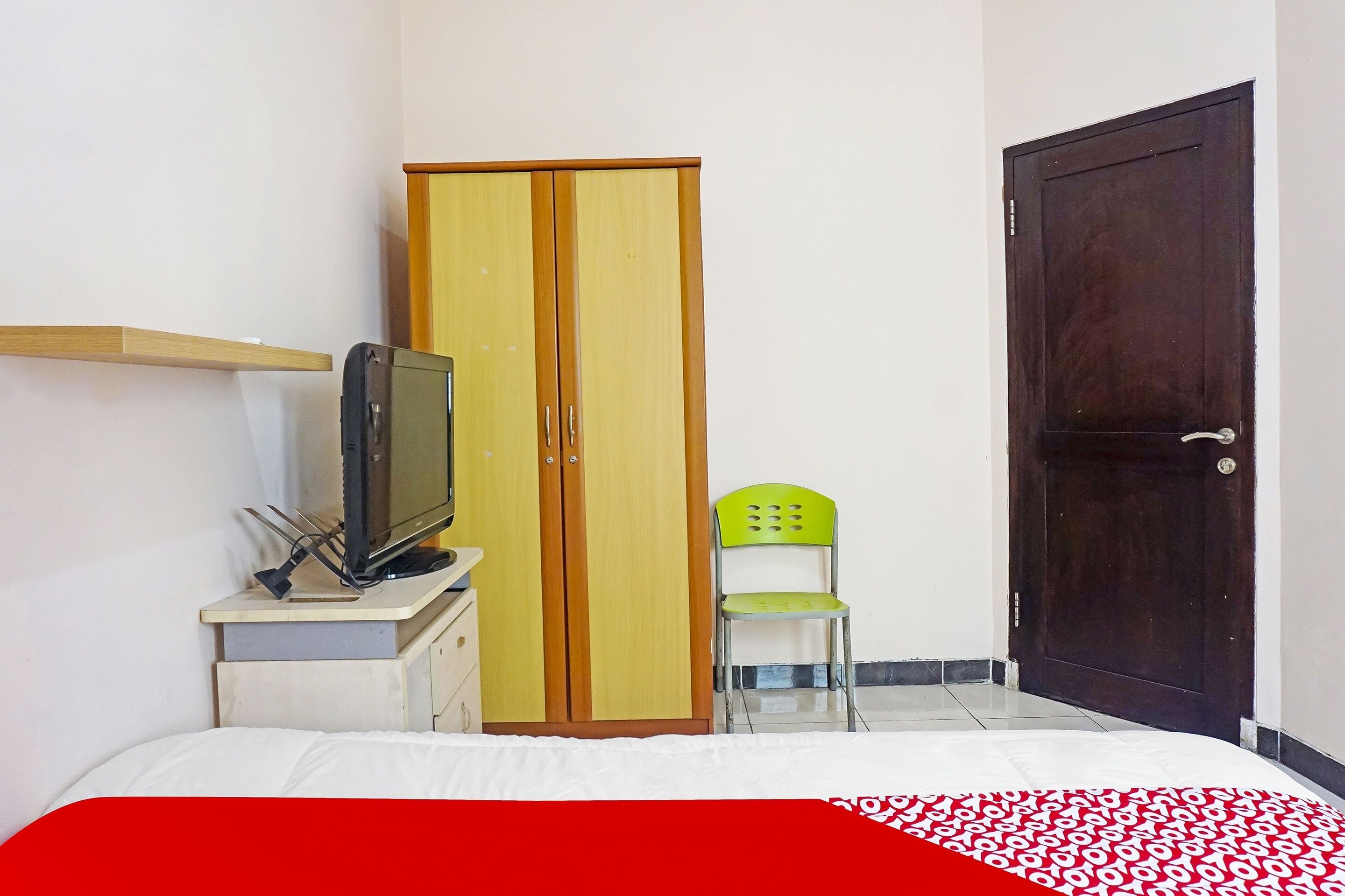 Ein Schlafzimmer mit einem Bett, einem Kleiderschrank, einem Fernseher auf einem Schrank und einem grünen Sessel.