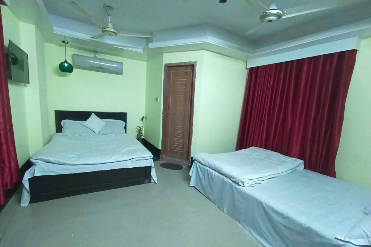 A room with two beds, a ceiling fan, an air conditioning unit, and a door.