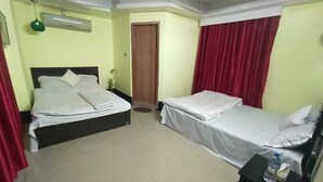 A hotel room with two beds, a small table, a water bottle, and a ceiling fan. - Hotel Relax Inn (Sylhet)