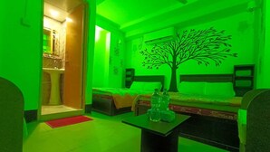 A room with a bed, a sofa, a table with water bottles, and a tree mural on the wall. - Hotel Relax Inn (Sylhet)