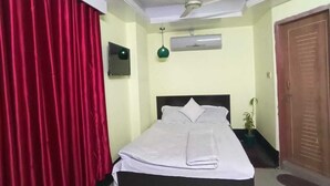 A neatly made bed with a white comforter and pillows, a ceiling fan, a wall-mounted air conditioner, and a wooden door. - Hotel Relax Inn (Sylhet)