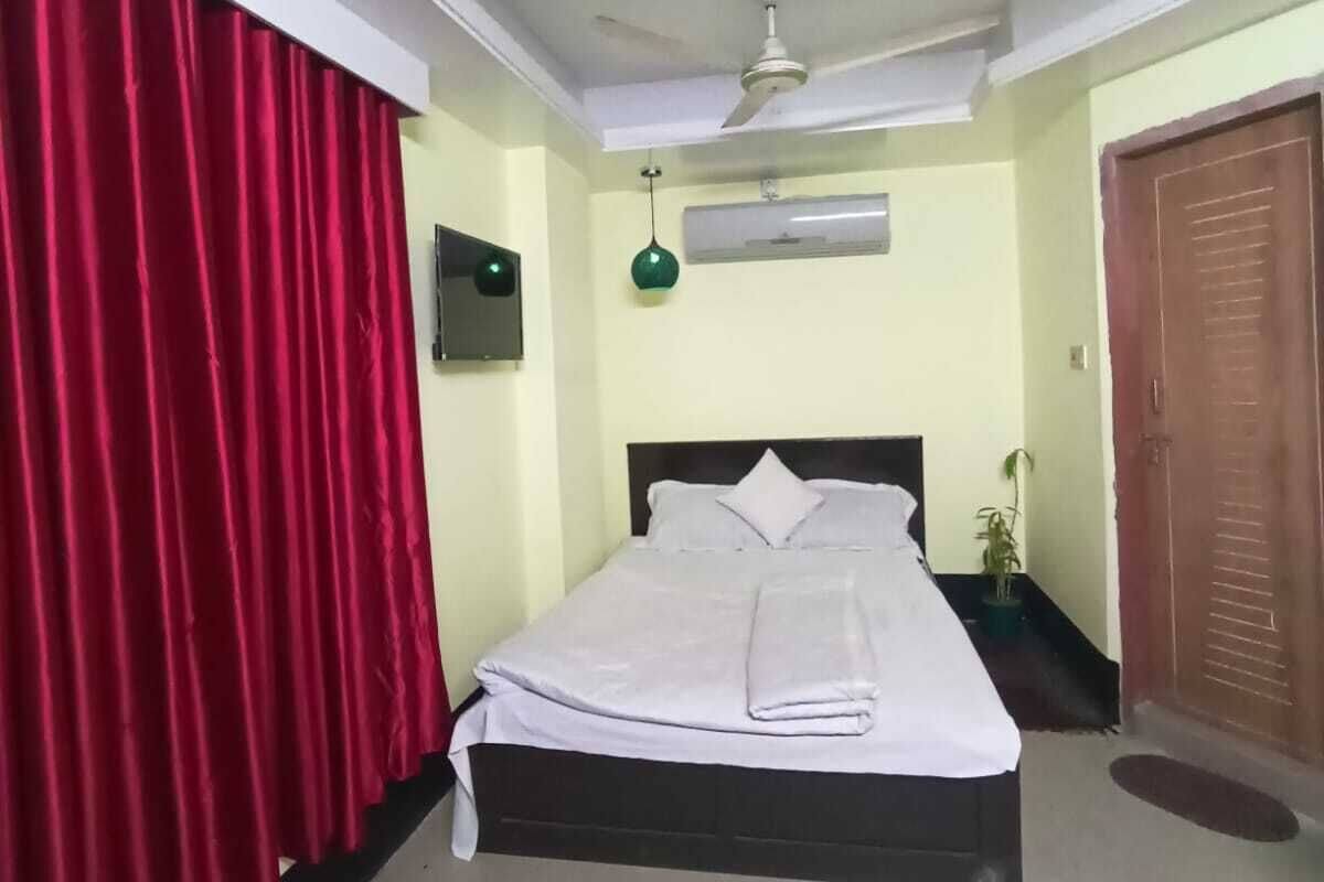 A neatly made bed with a white comforter and pillows, a ceiling fan, a wall-mounted air conditioner, and a wooden door.