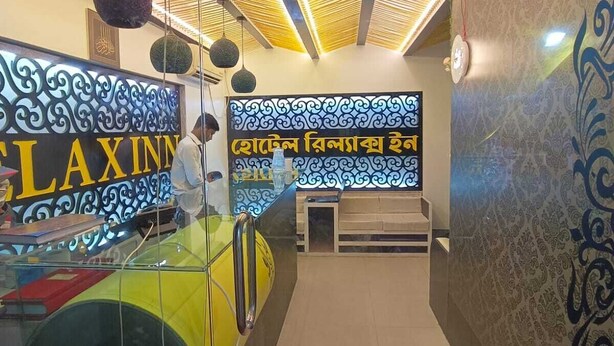 A hotel reception area with a modern design, featuring a reception desk, a wall with decorative patterns, and a ceiling with geometric light fixtures. - Hotel Relax Inn (Sylhet)