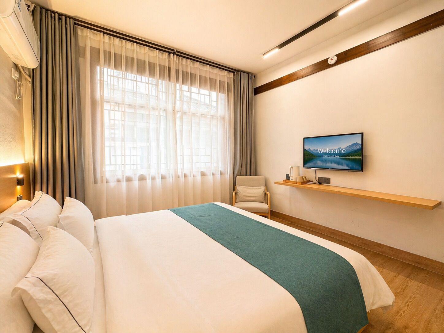 Een hotelkamer met een bed, een stoel, een televisie aan de muur en een raam met gordijnen.