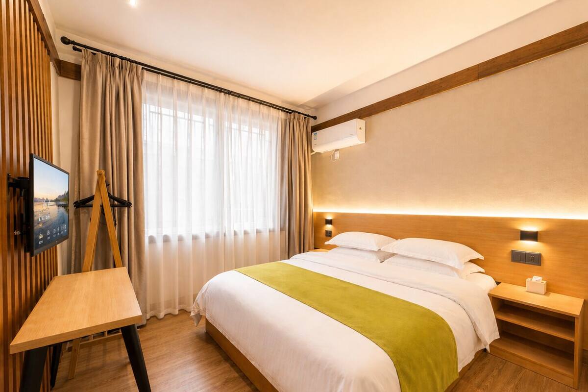 A hotel room with a bed, a desk, a TV, and a window with curtains.