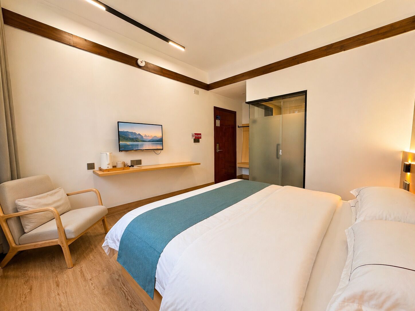 A hotel room with a bed, a chair, a TV, a shelf, and a wardrobe.