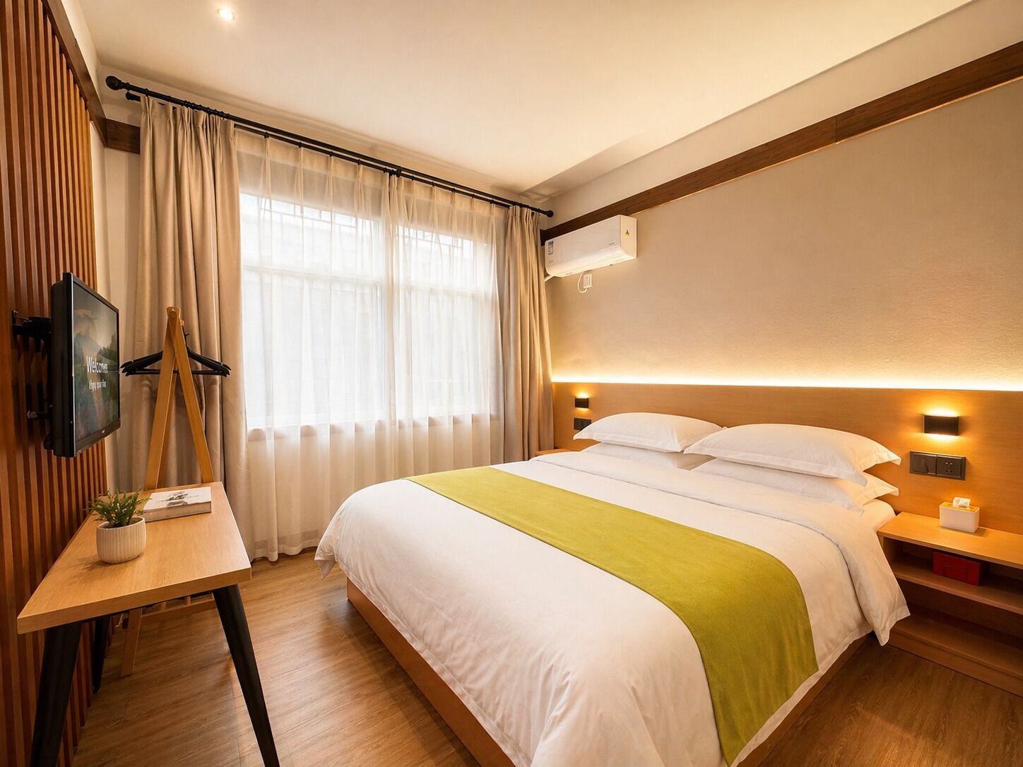 Een hotelkamer met een bed, een bureau met een plant, een televisie en een raam met gordijnen.