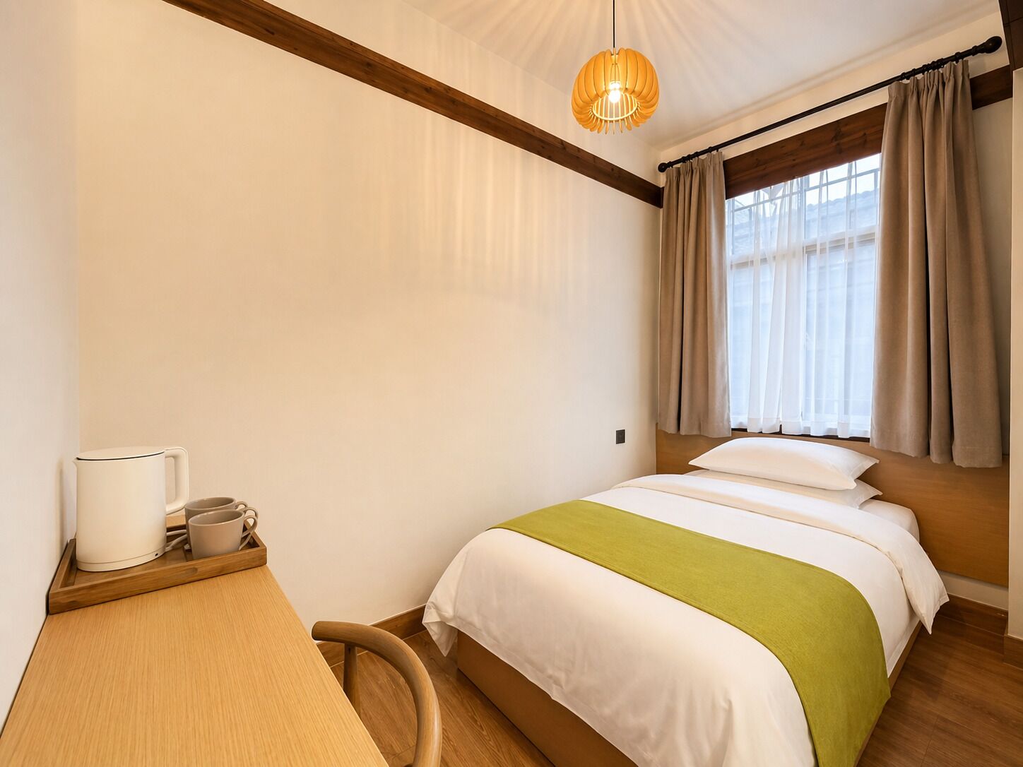 A bedroom with a bed, a desk with a chair, a hanging light fixture, and a window with curtains.