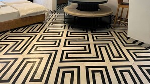 A room with a geometric patterned floor, a bed with white linens, and a round table with a black base.