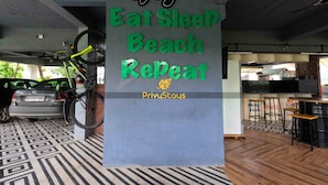 A sign with the text "St. Rikey's Eat Sleep Beach Repeat" and "PrivyStays" in a modern indoor setting with a bicycle, a car, and a bar area.