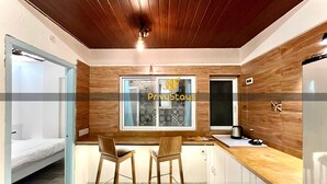 A modern kitchen with wooden cabinets, a built-in oven, and a window with patterned curtains.