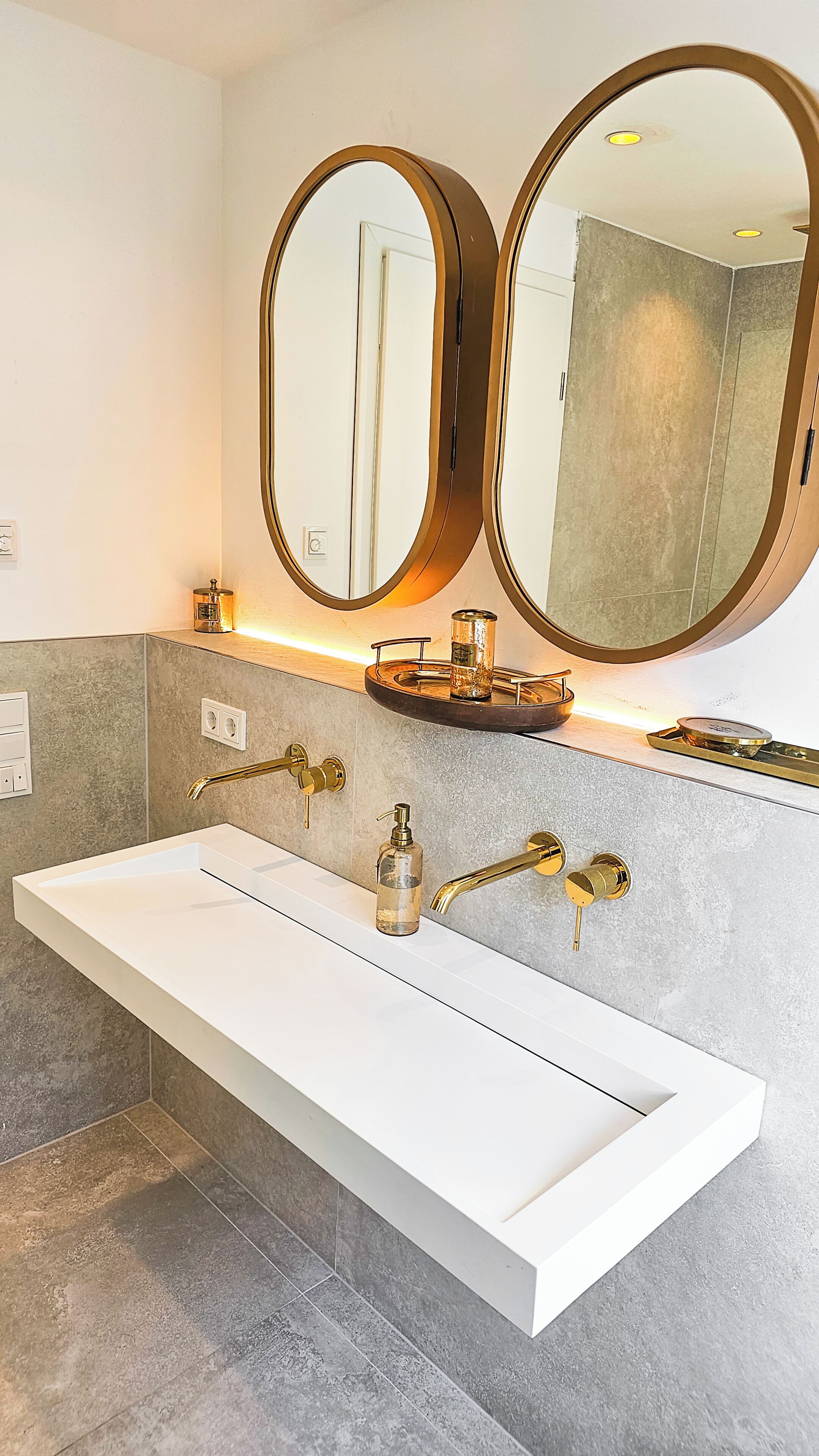 Un baño moderno con un tocador blanco, dos espejos grandes y un grifo dorado.